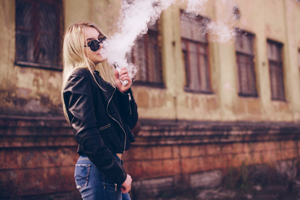 Beautiful woman vaping vapor outdoors